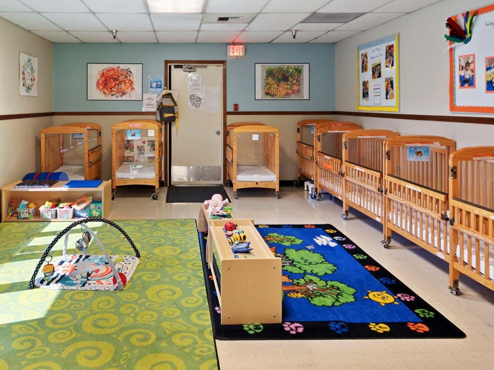 daycare classroom with multiple cribs, an infant playmat, and colorful rugs