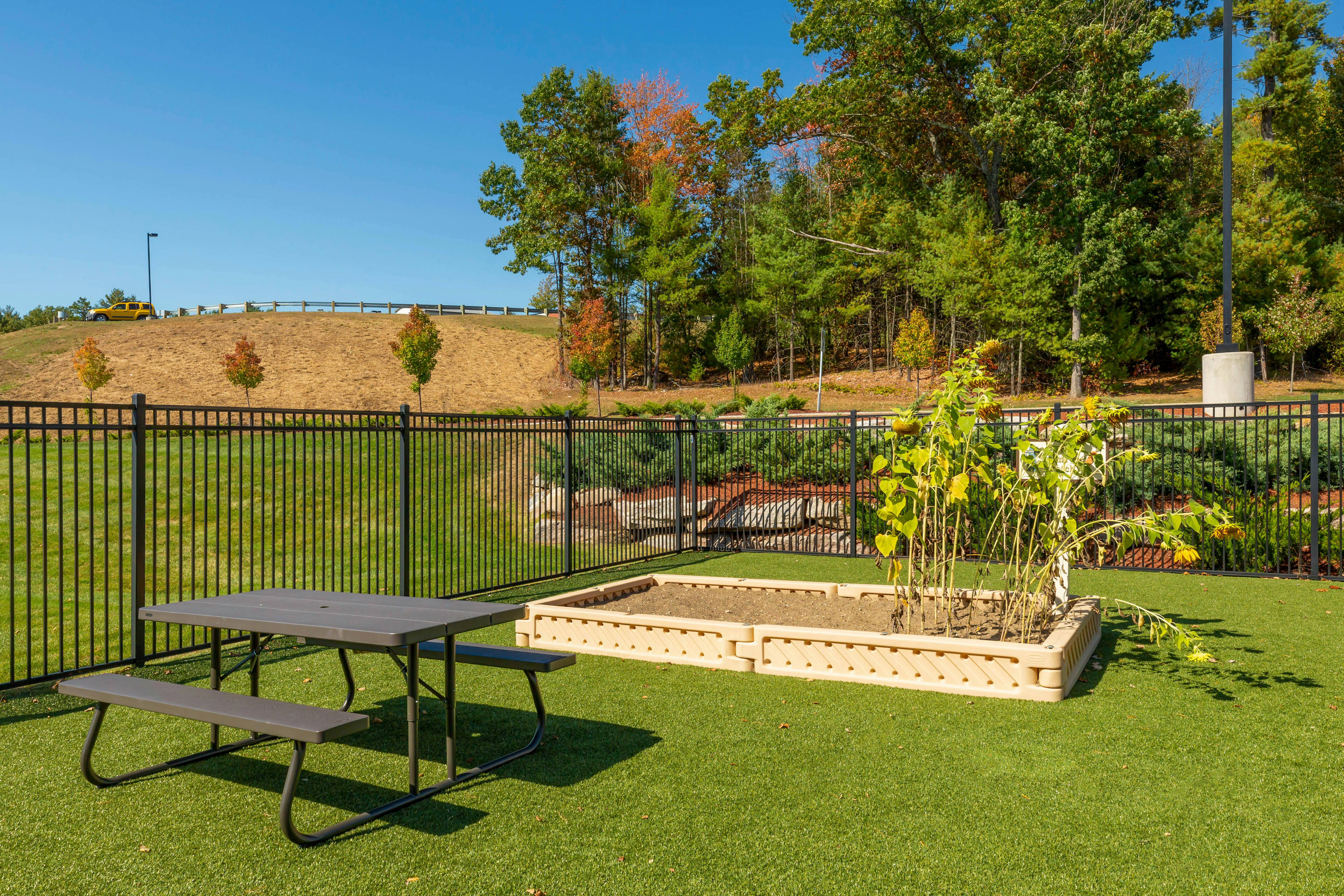 Picnic table on artificial turf next to a raised garden bed with sunflowers