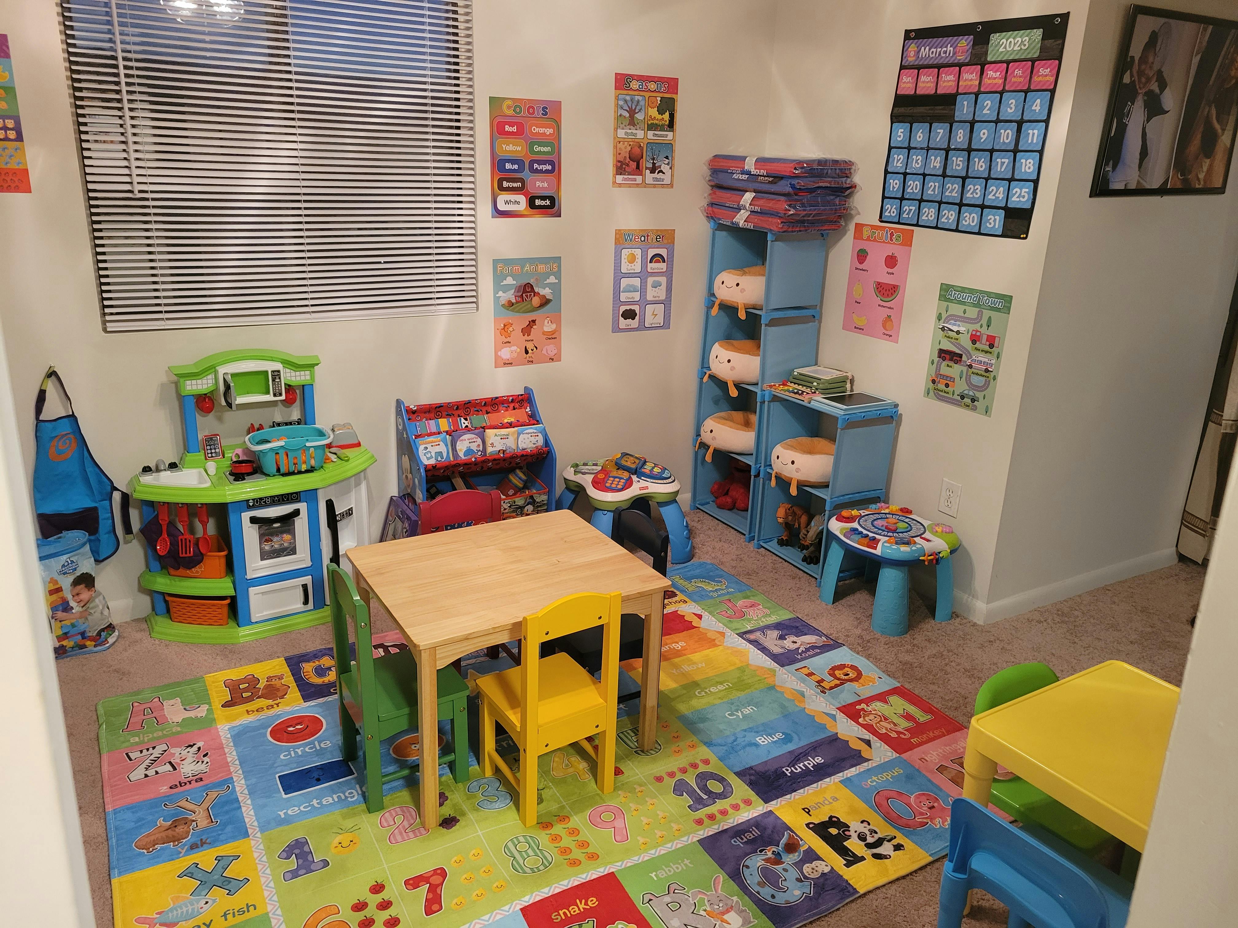 A playroom with a small wooden table and chairs on a colorful alphabet rug