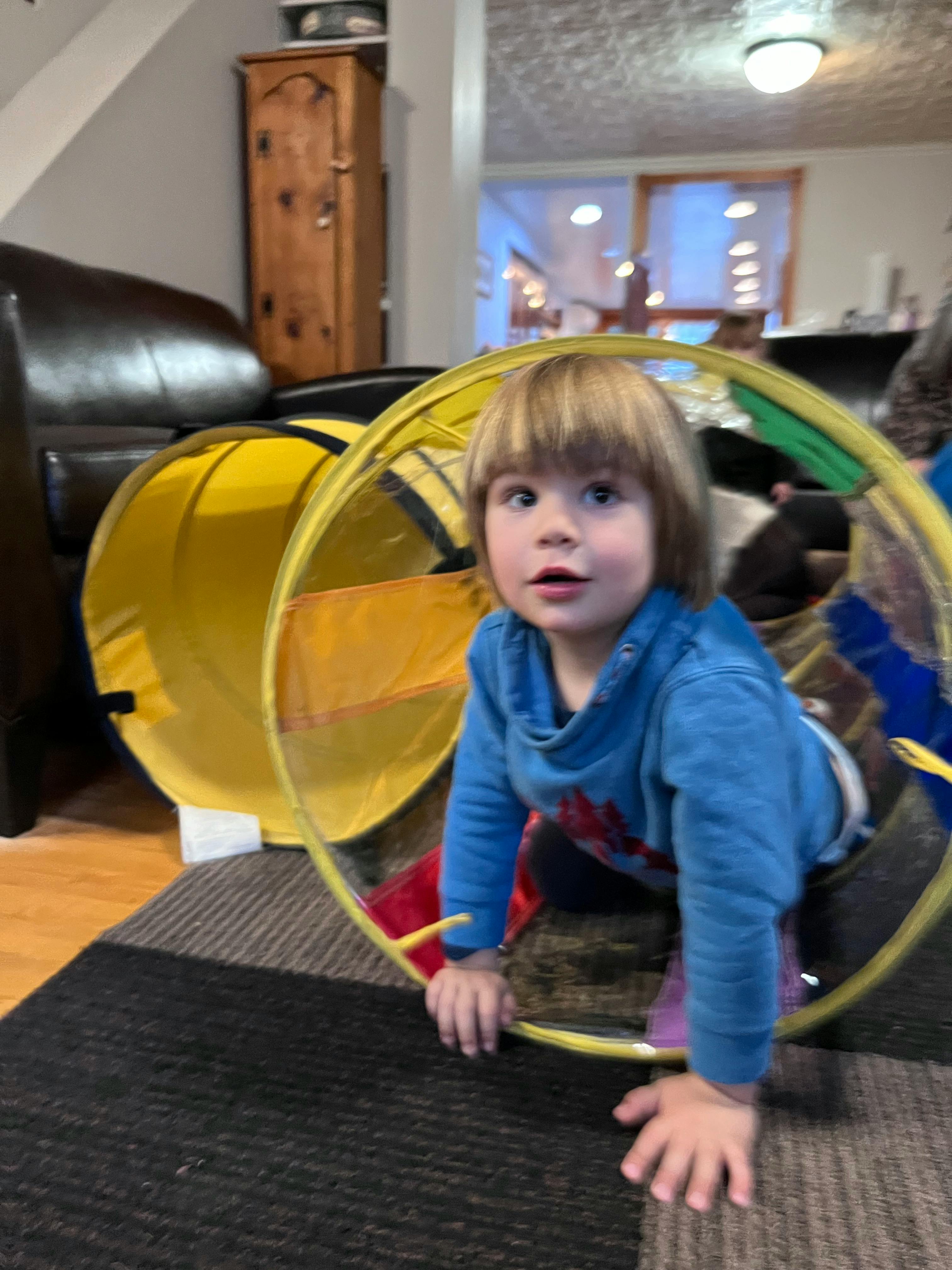 Child crawling through a yellow play tunnel