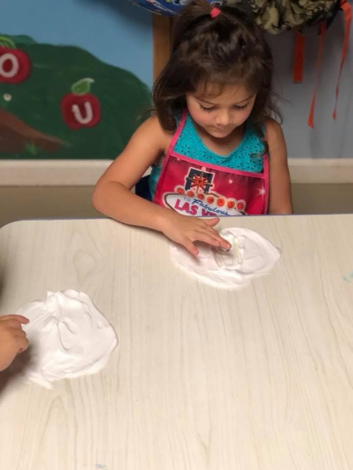 Child in an apron playing with white slime on a table