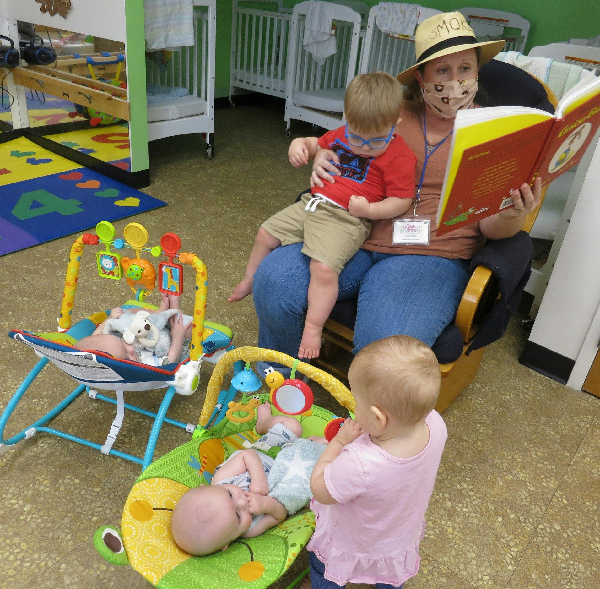Person reading a book to a child, with other children nearby