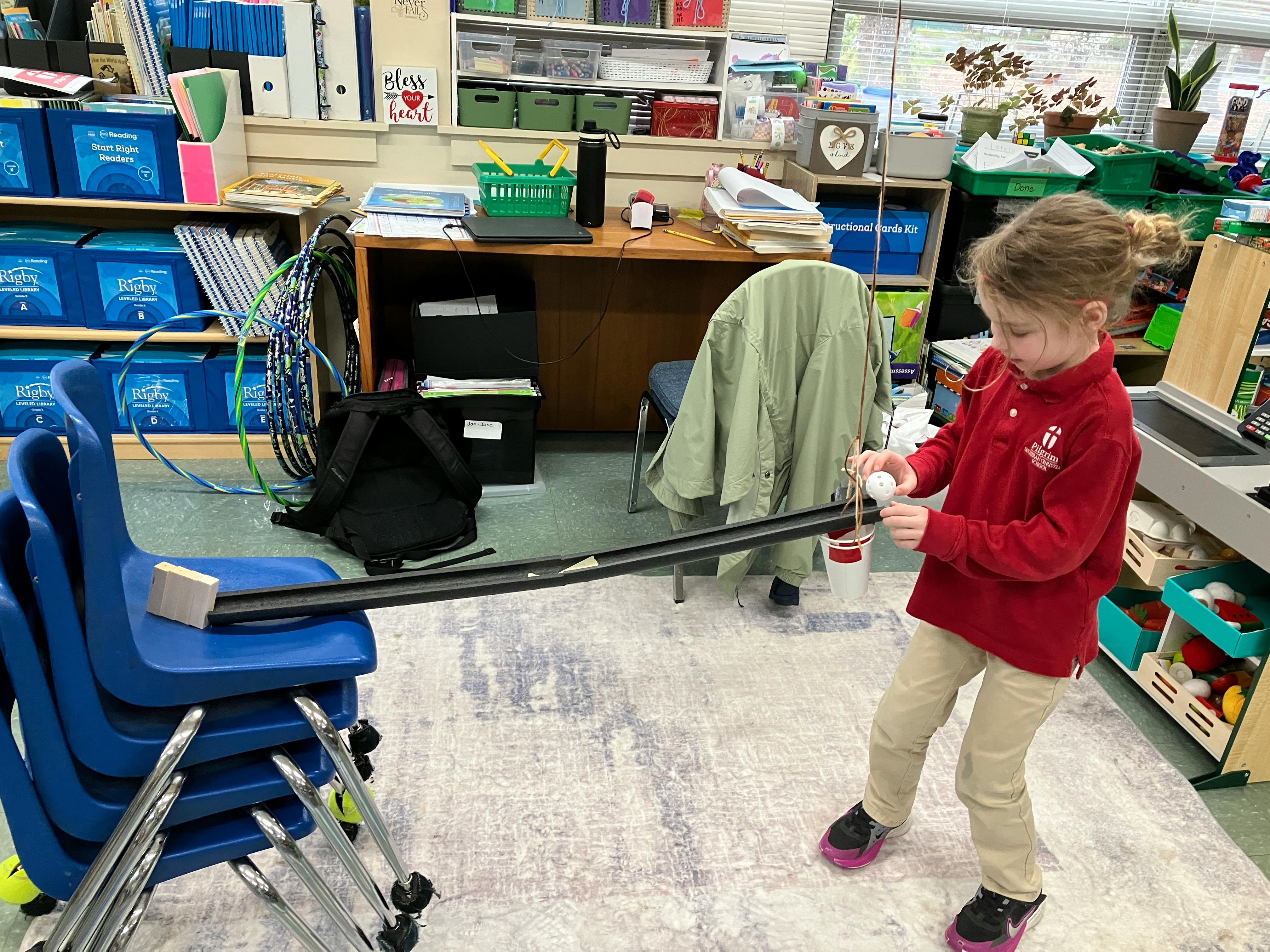 child in a classroom dropping a white ball into a track leading to a bucket