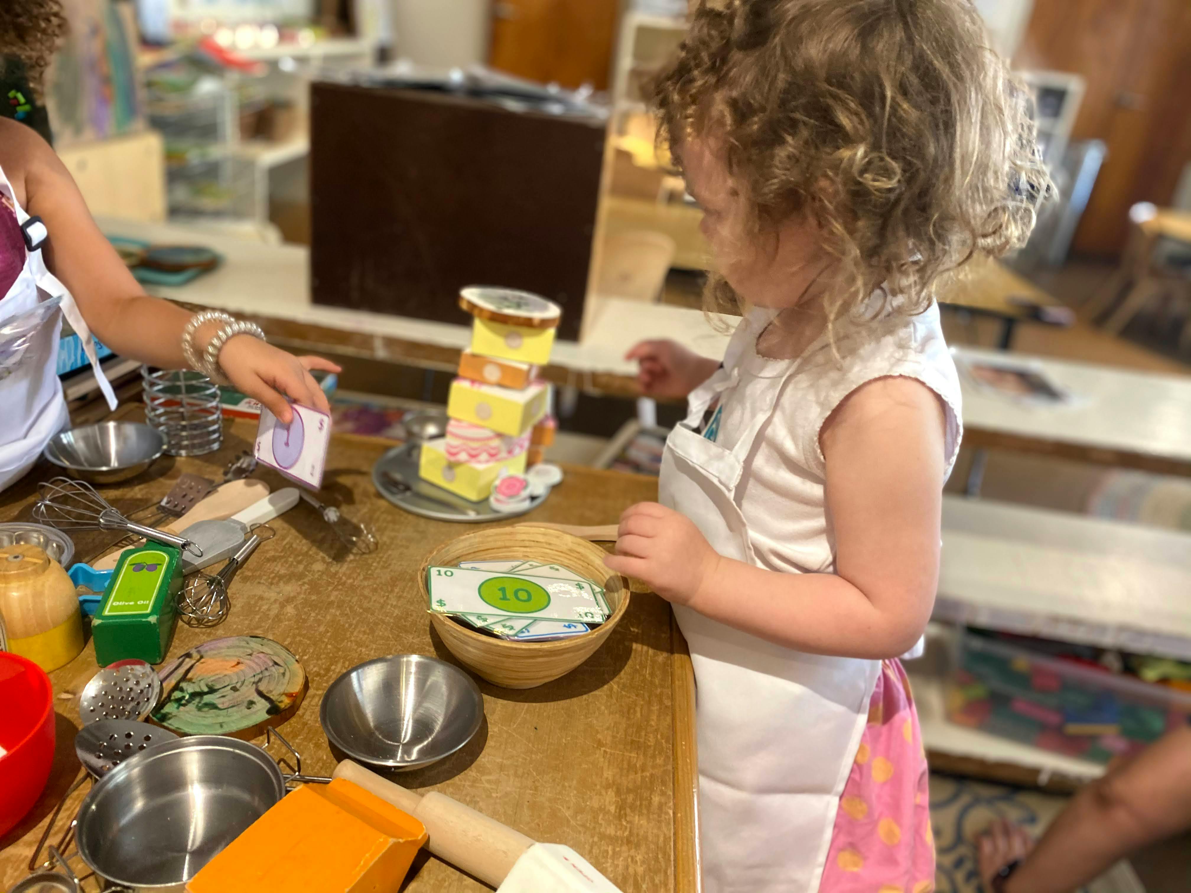 Child and person in aprons at a table with bowls and play food