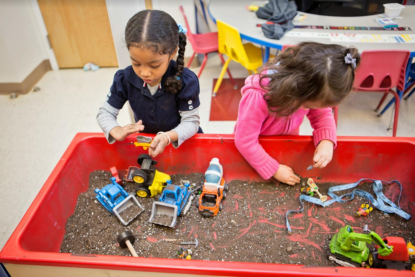 Two children playing with toy trucks in a sandbox
