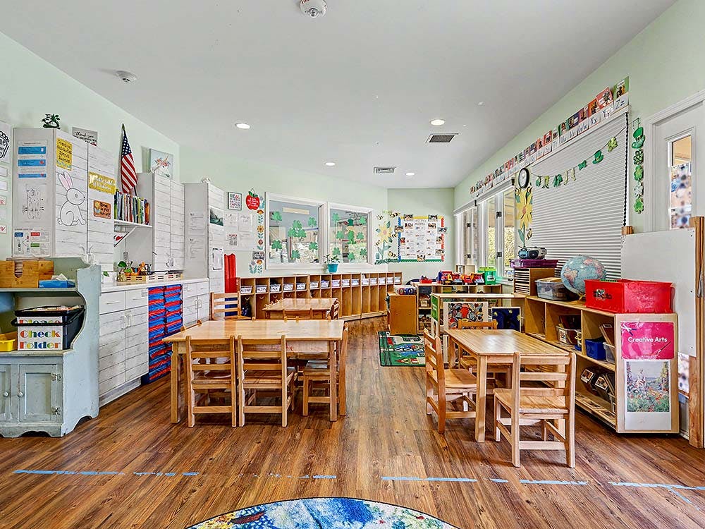 Empty classroom with small wooden tables and chairs, shelves, and decorations