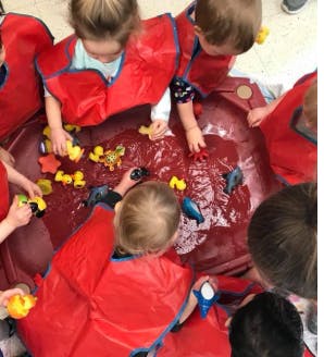Children in red smocks playing with toys in a water table