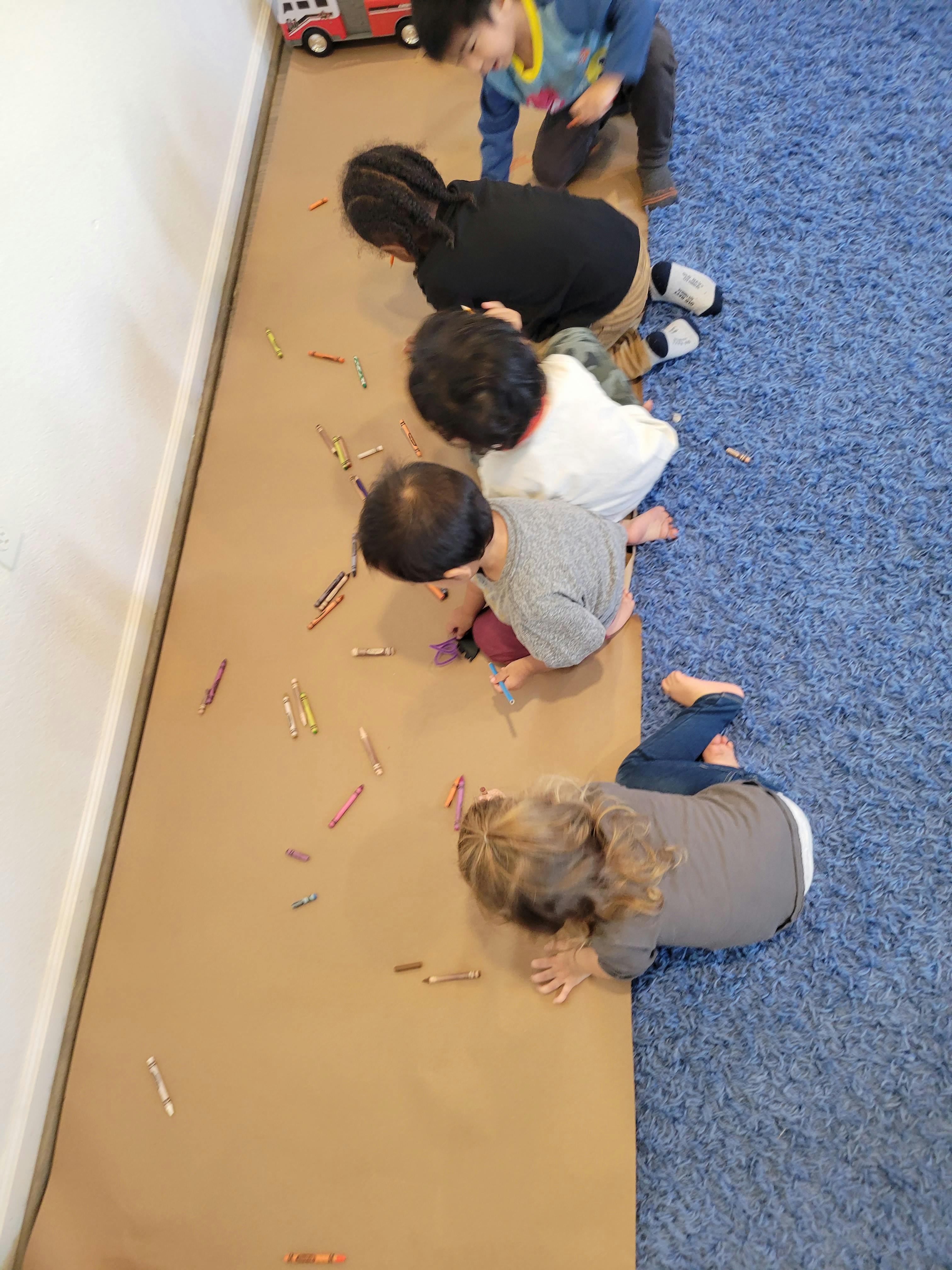 Group of children drawing with crayons on a large sheet of paper on the floor