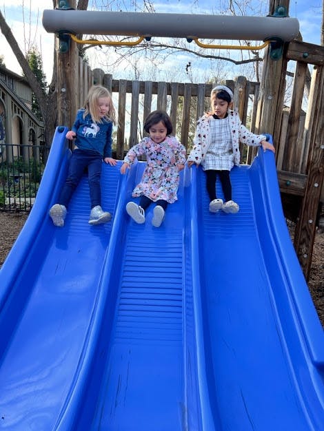 Three children sitting on blue slides on a playground