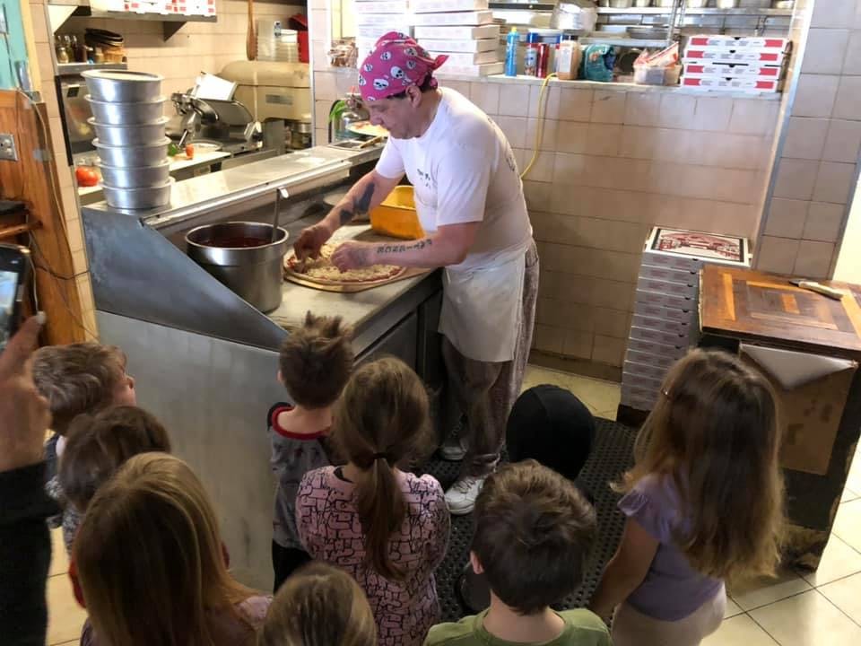 Person making pizza for a group of children