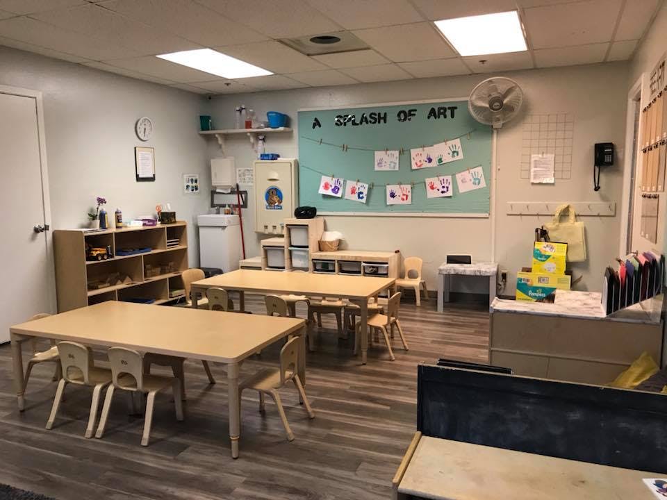 Classroom with small tables and chairs, shelves, and a bulletin board with art
