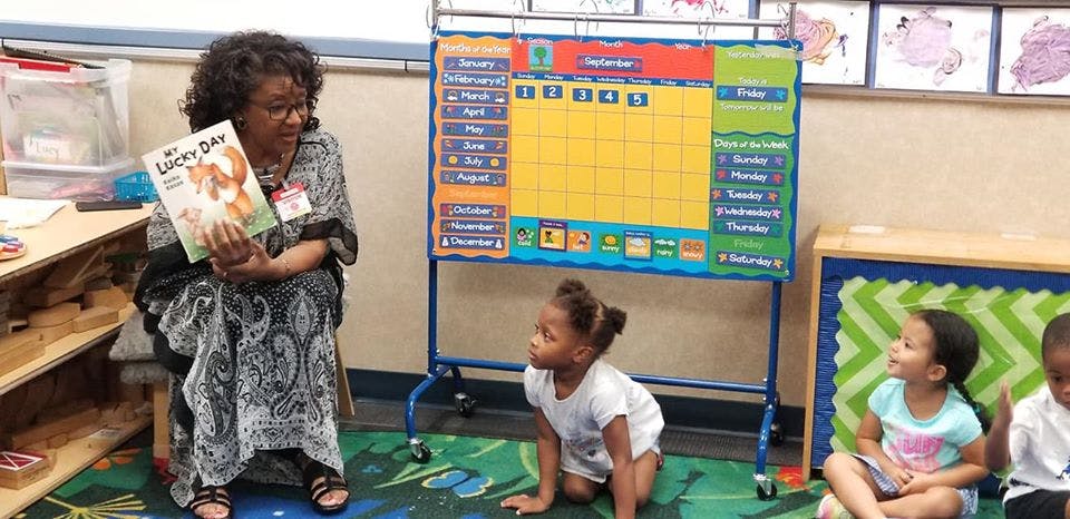 Person holding a book and reading to children in a classroom