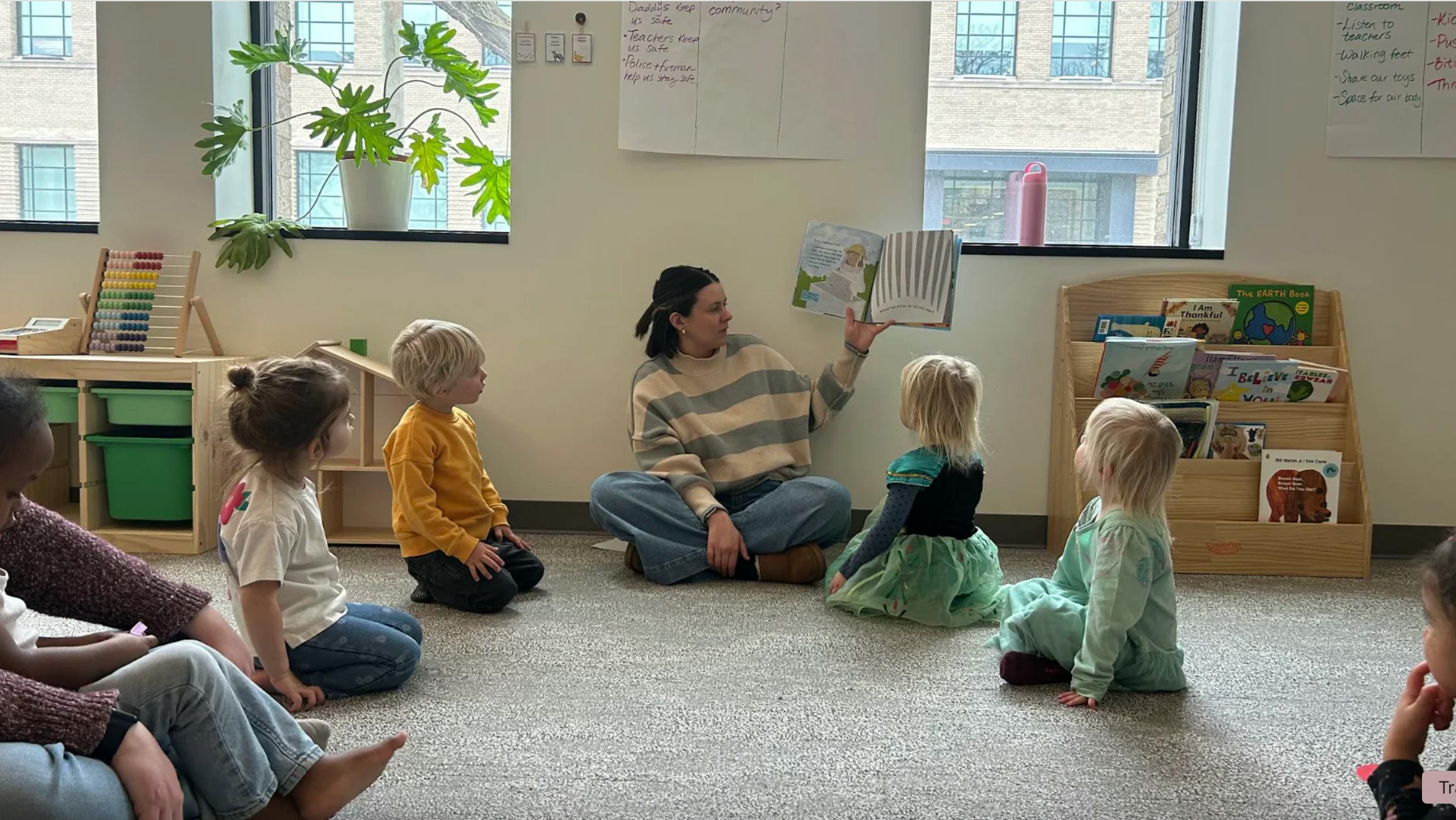 Adult person reading a book to several children in a classroom setting