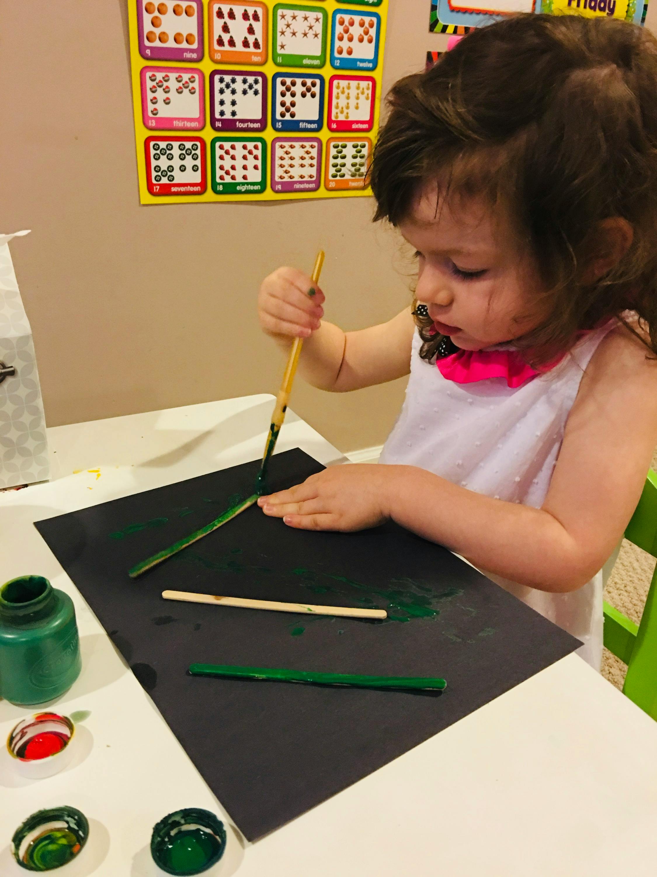 Child painting sticks green on a black paper