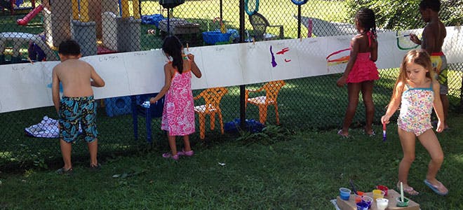 Children painting on a long white board outdoors