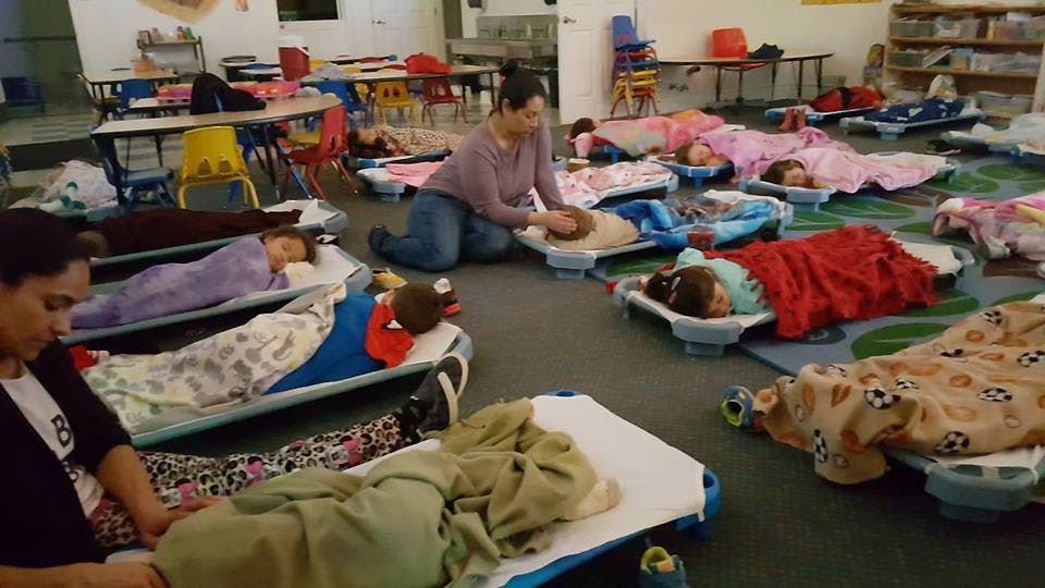 Adults supervising children sleeping on cots in a room