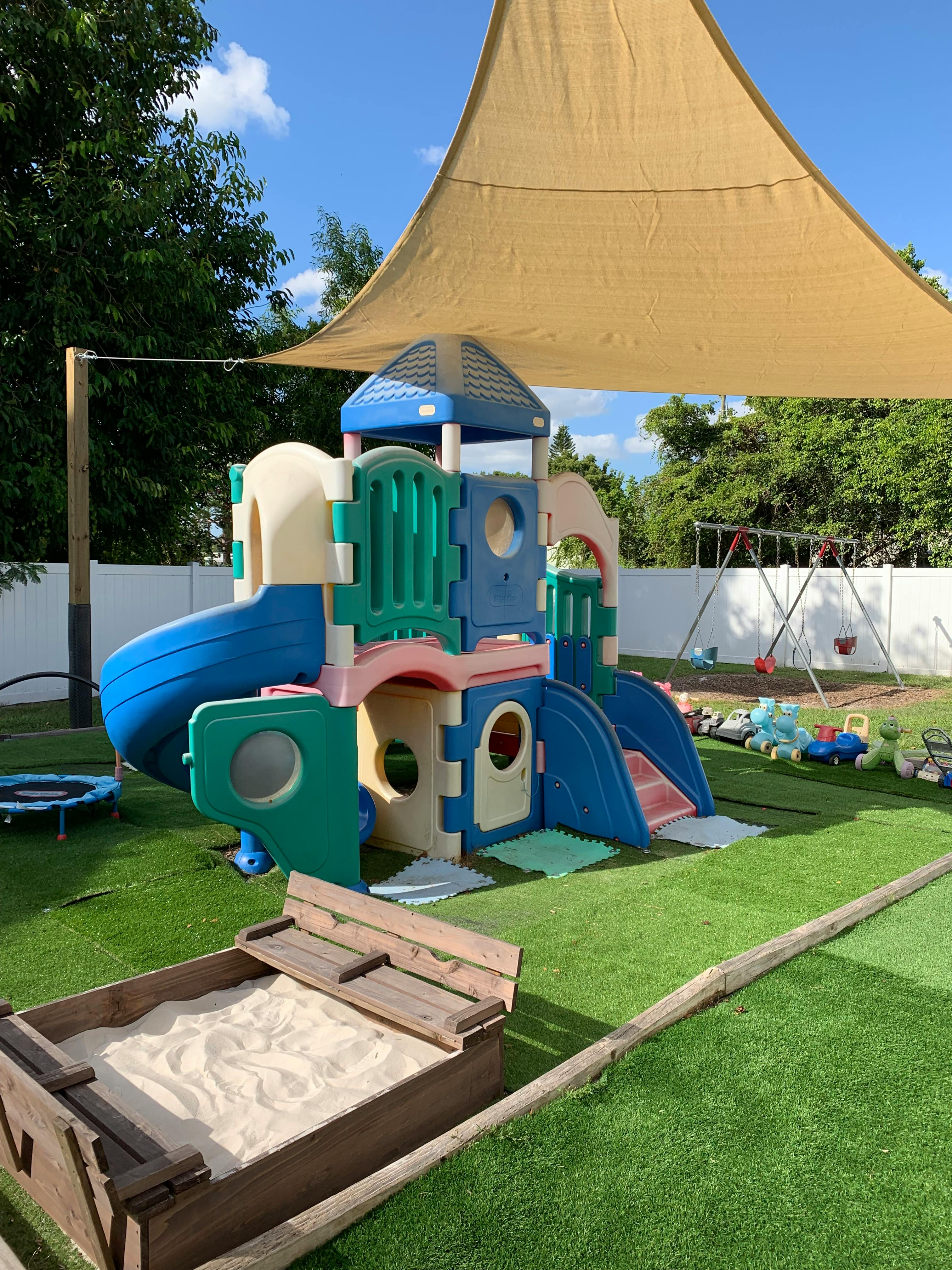 Playground with a colorful play structure, sandbox, and swing set under a shade sail