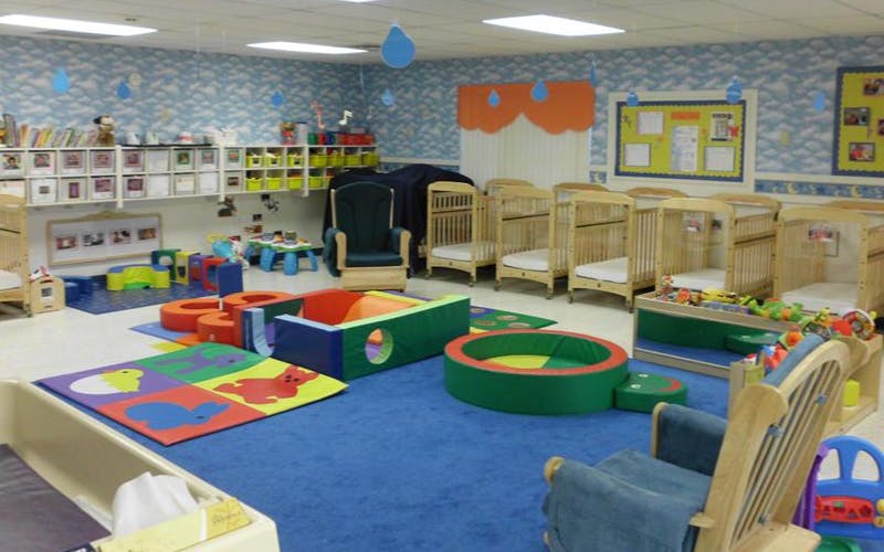 A colorful childcare room with cribs, play mats, and soft play structures