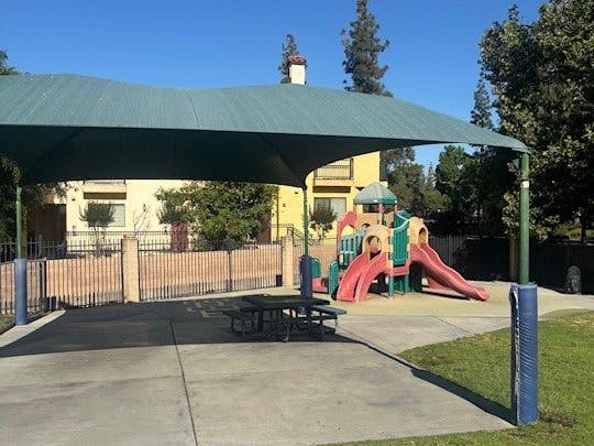 Playground with slides under a large shade canopy next to picnic tables