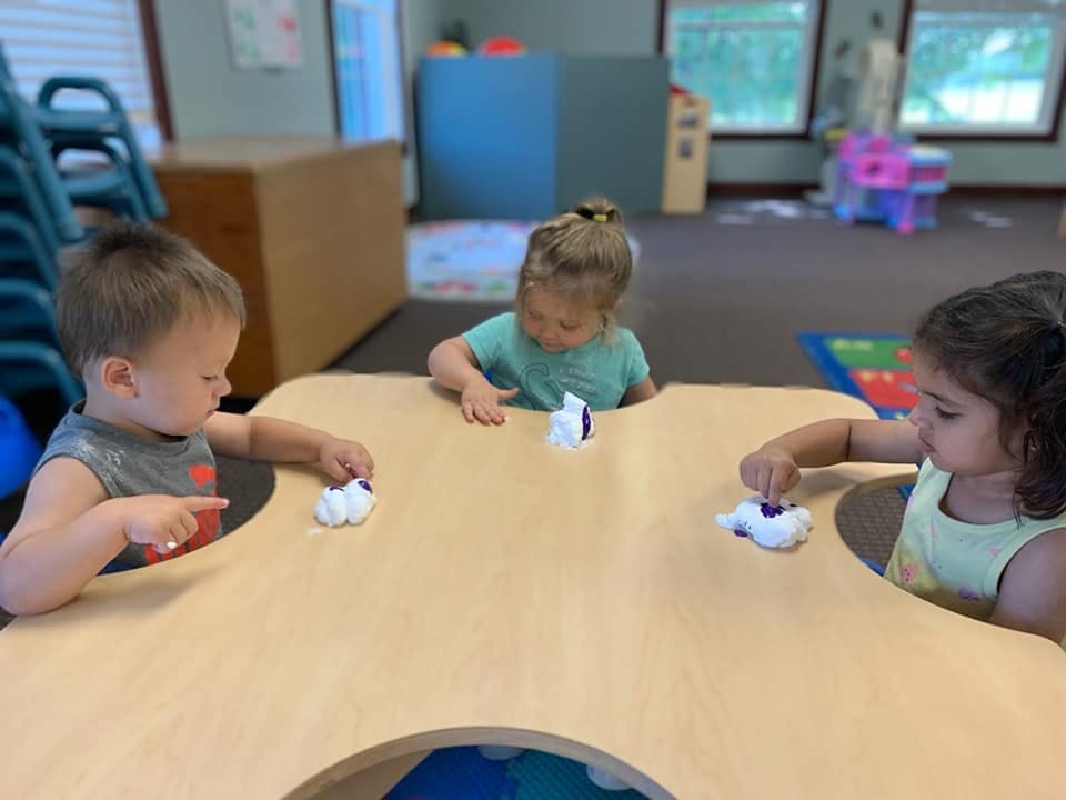 Three children playing with objects at a table