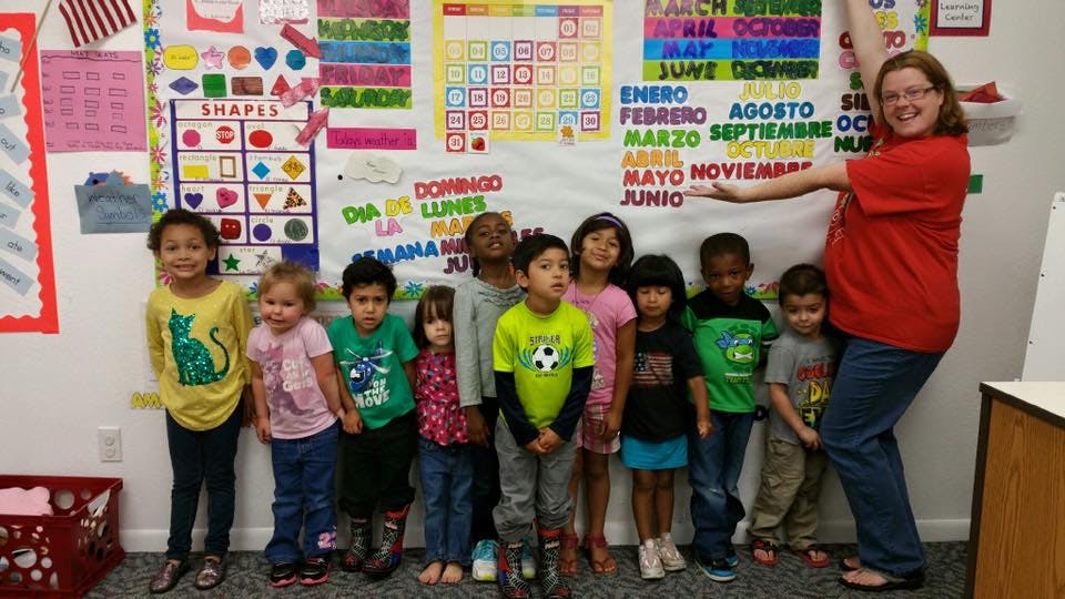 Adult and group of children standing in front of a classroom wall display