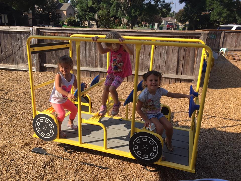 Three children playing on a yellow bus-shaped playground structure