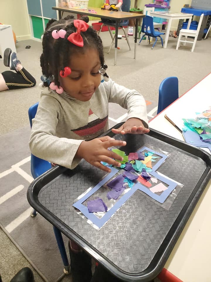 Child making a cross craft with colorful tissue paper