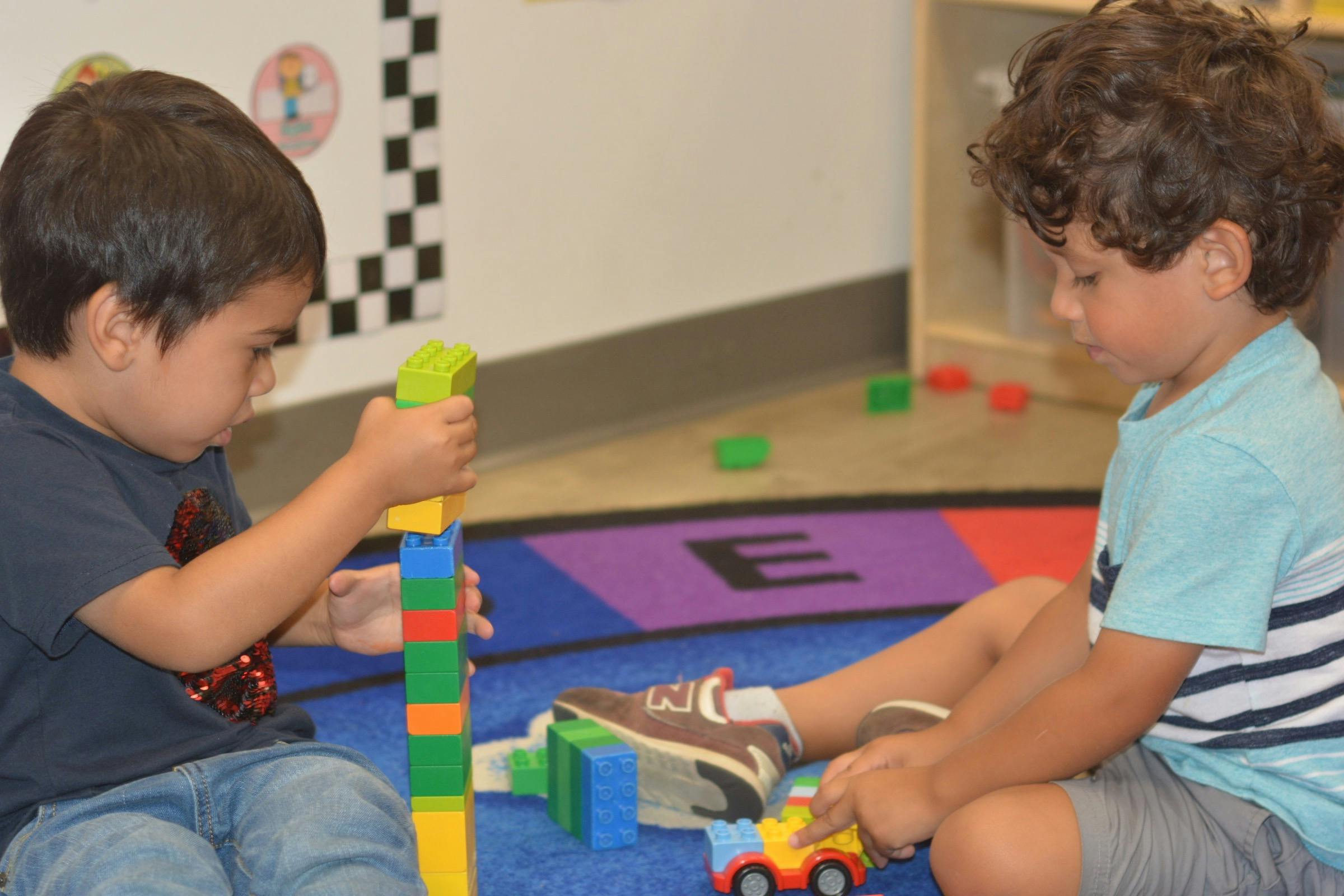Two children playing with colorful building blocks on a rug
