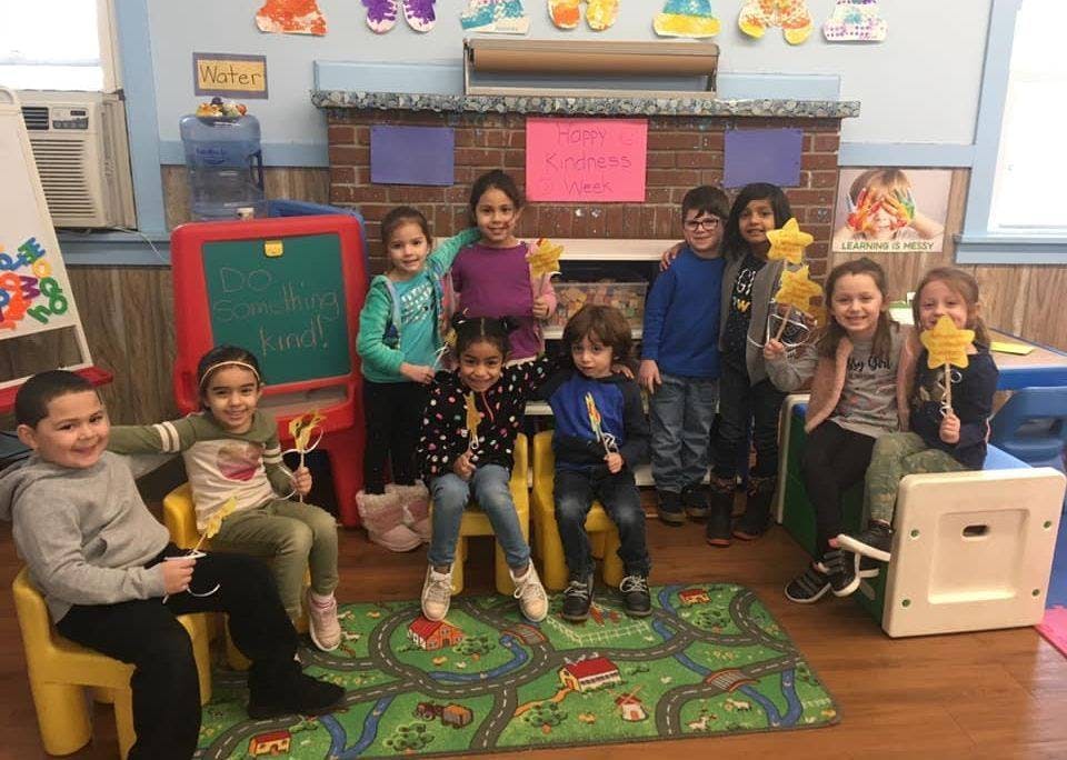 Group of children posing in a classroom, some holding star-shaped objects