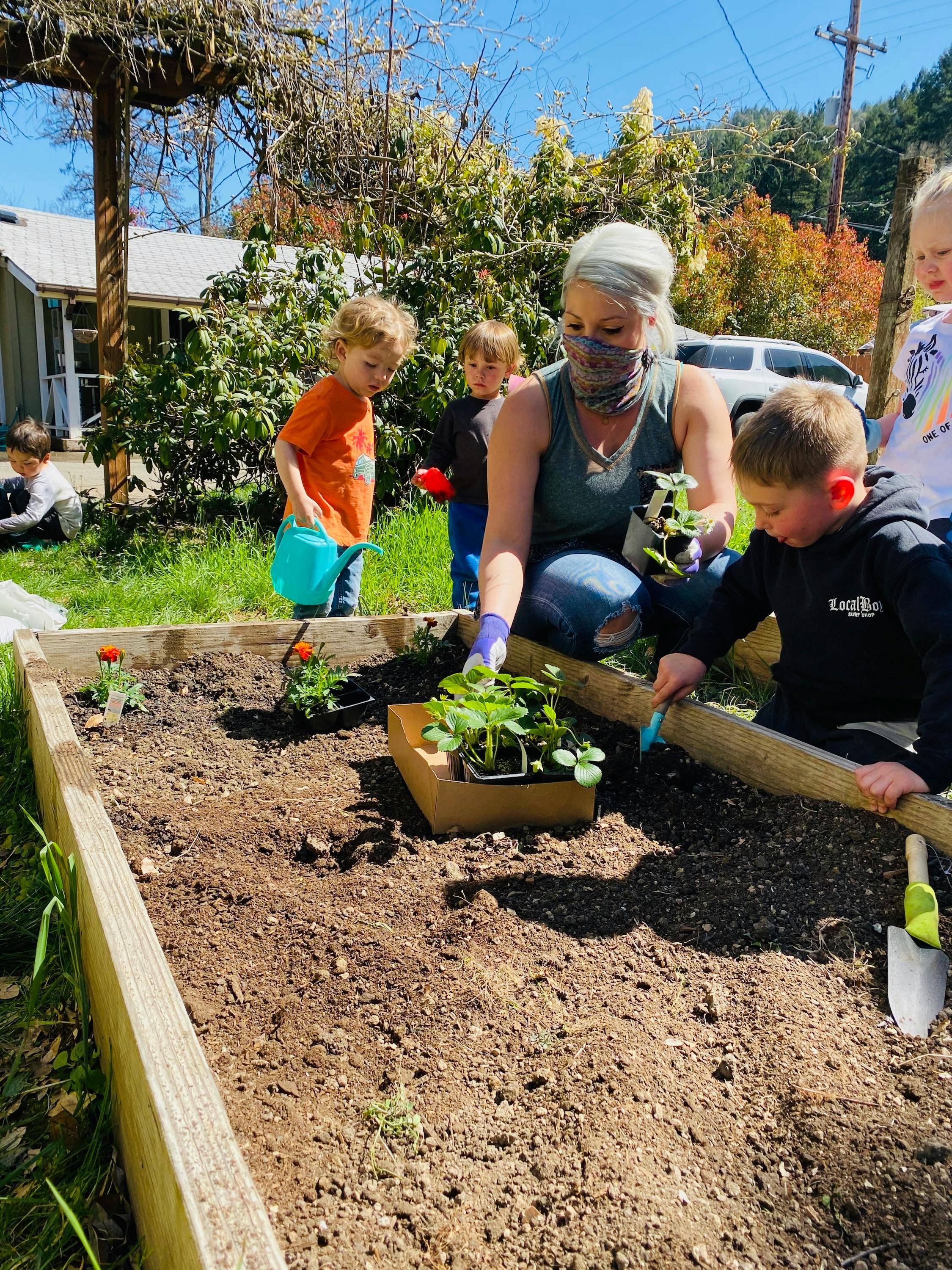Person and children planting in a raised garden bed
