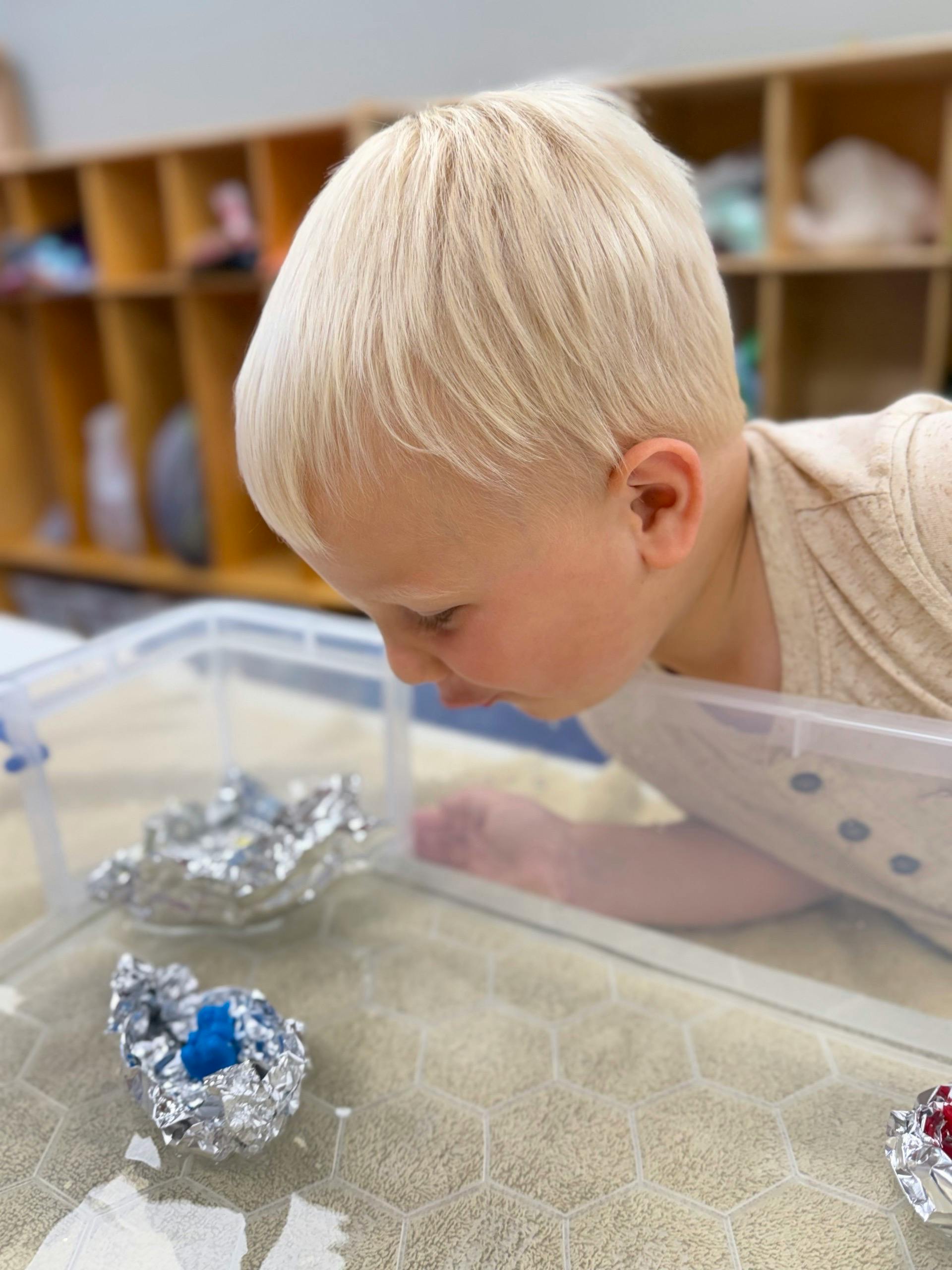 Child looking closely at aluminum foil boats in a plastic bin