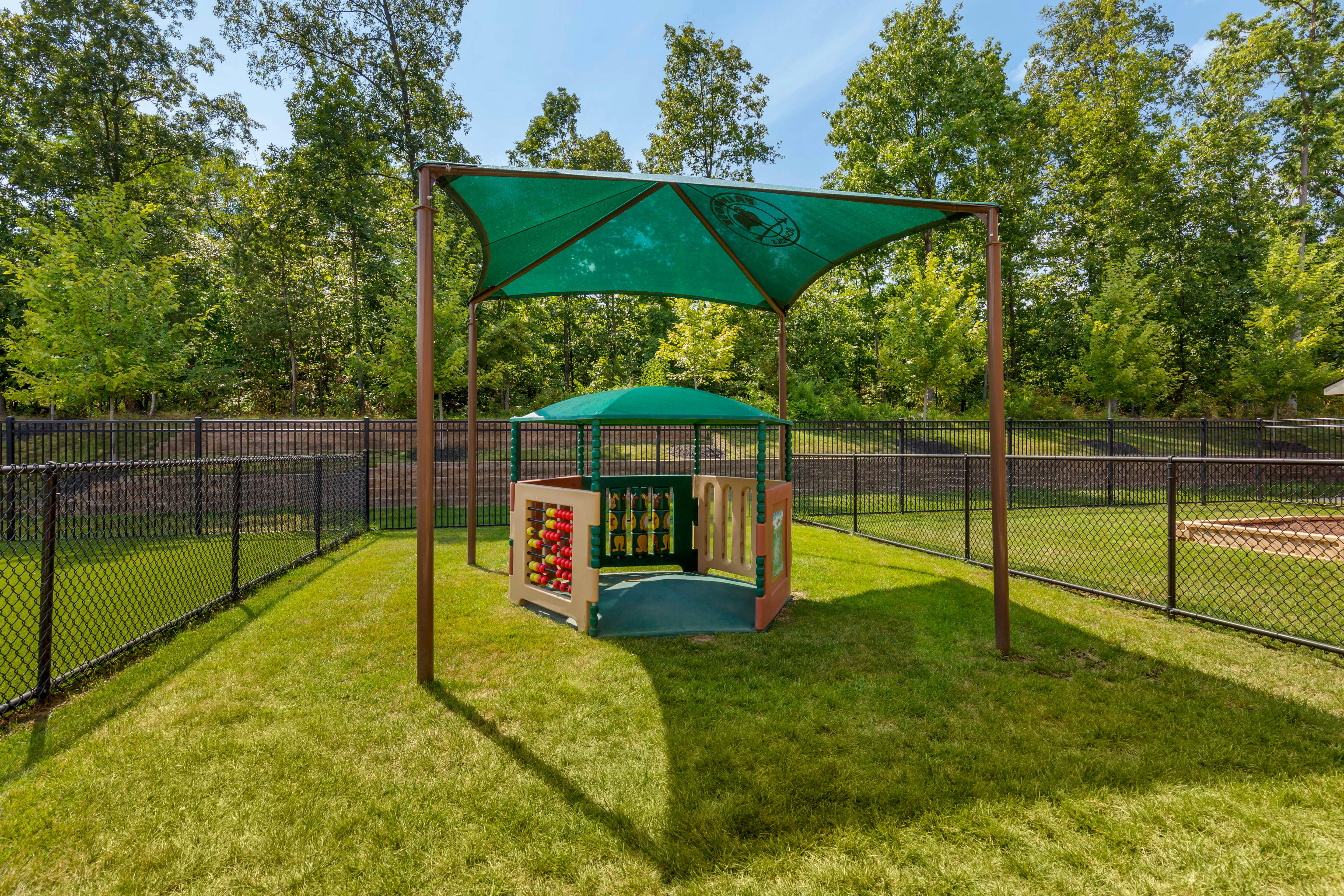 Fenced playground with a shaded play structure on green grass
