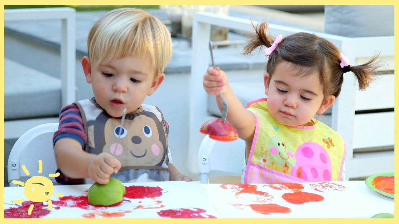 Two children in bibs playing with food at a table