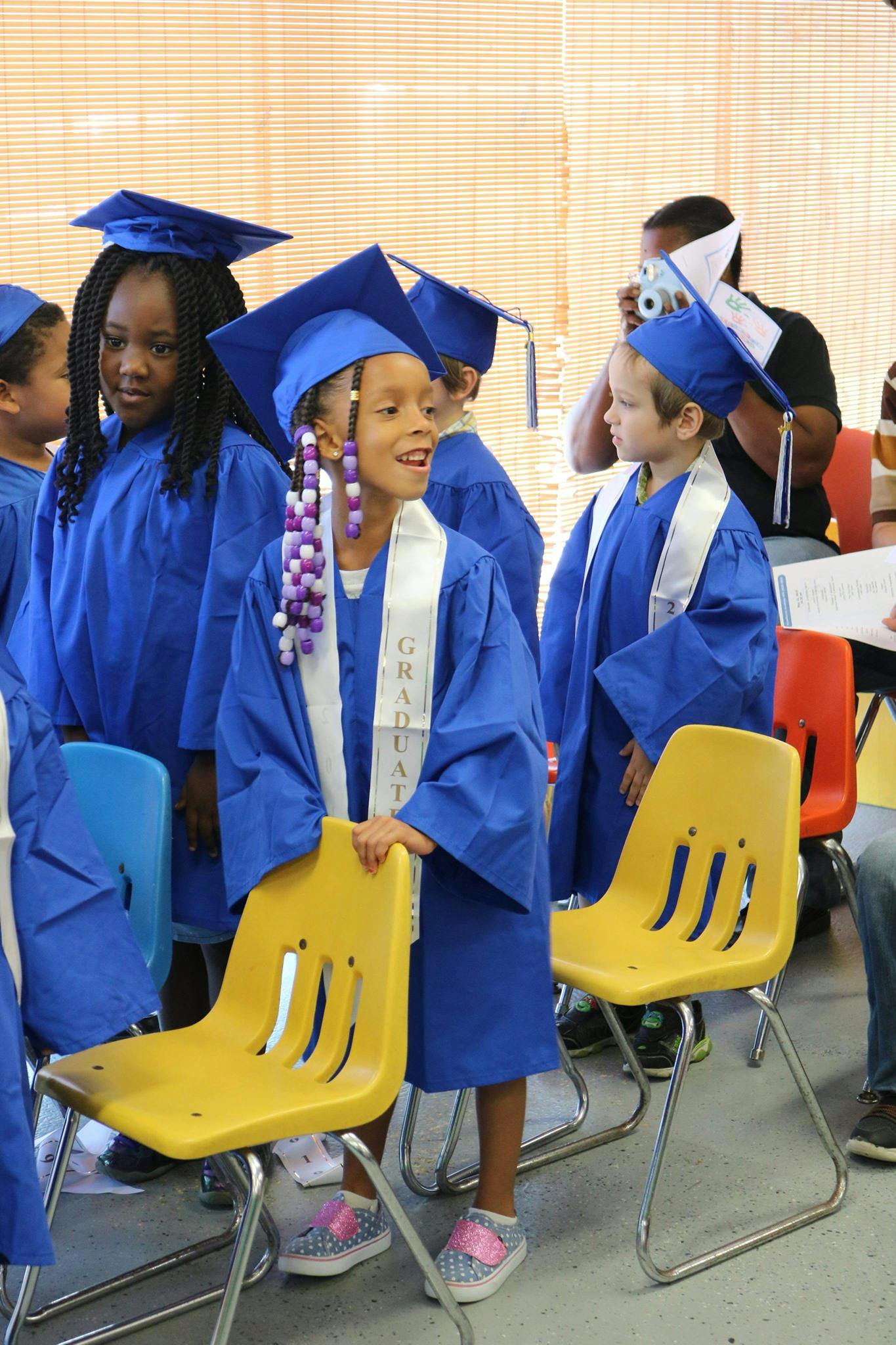 Children in blue graduation caps and gowns standing in a room