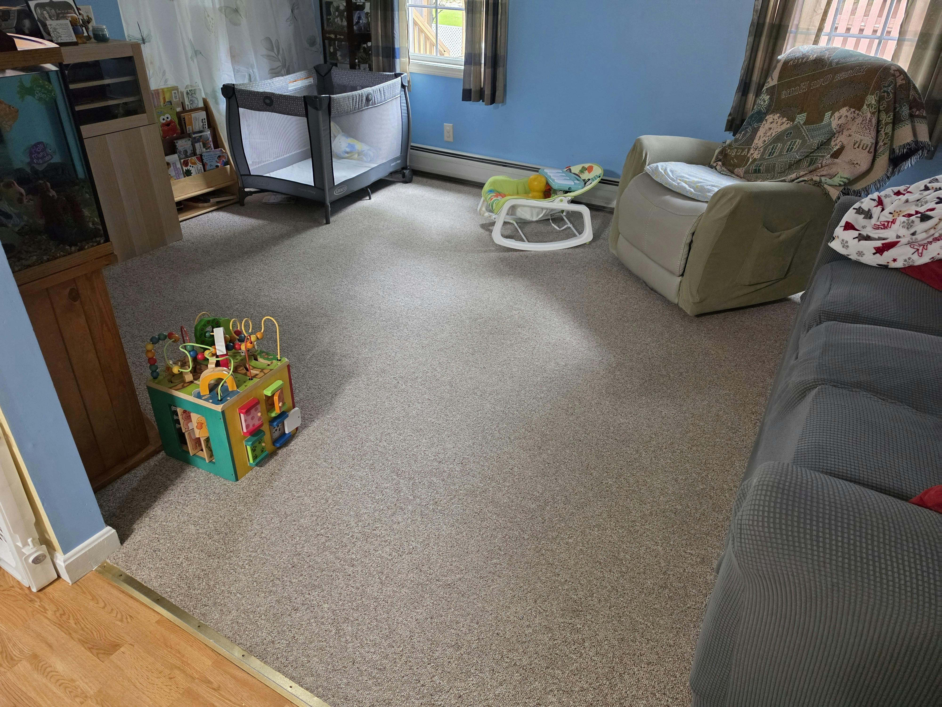 Playpen, infant bouncer, activity cube, and couch in a carpeted room
