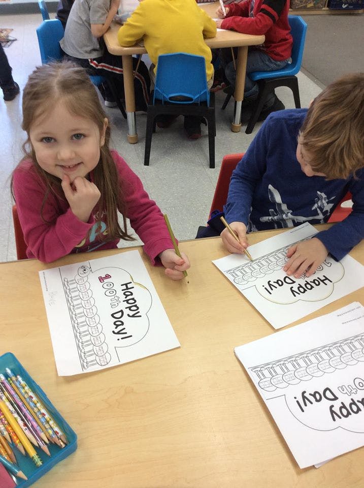 Child coloring a "Happy 100th Day!" worksheet in a classroom