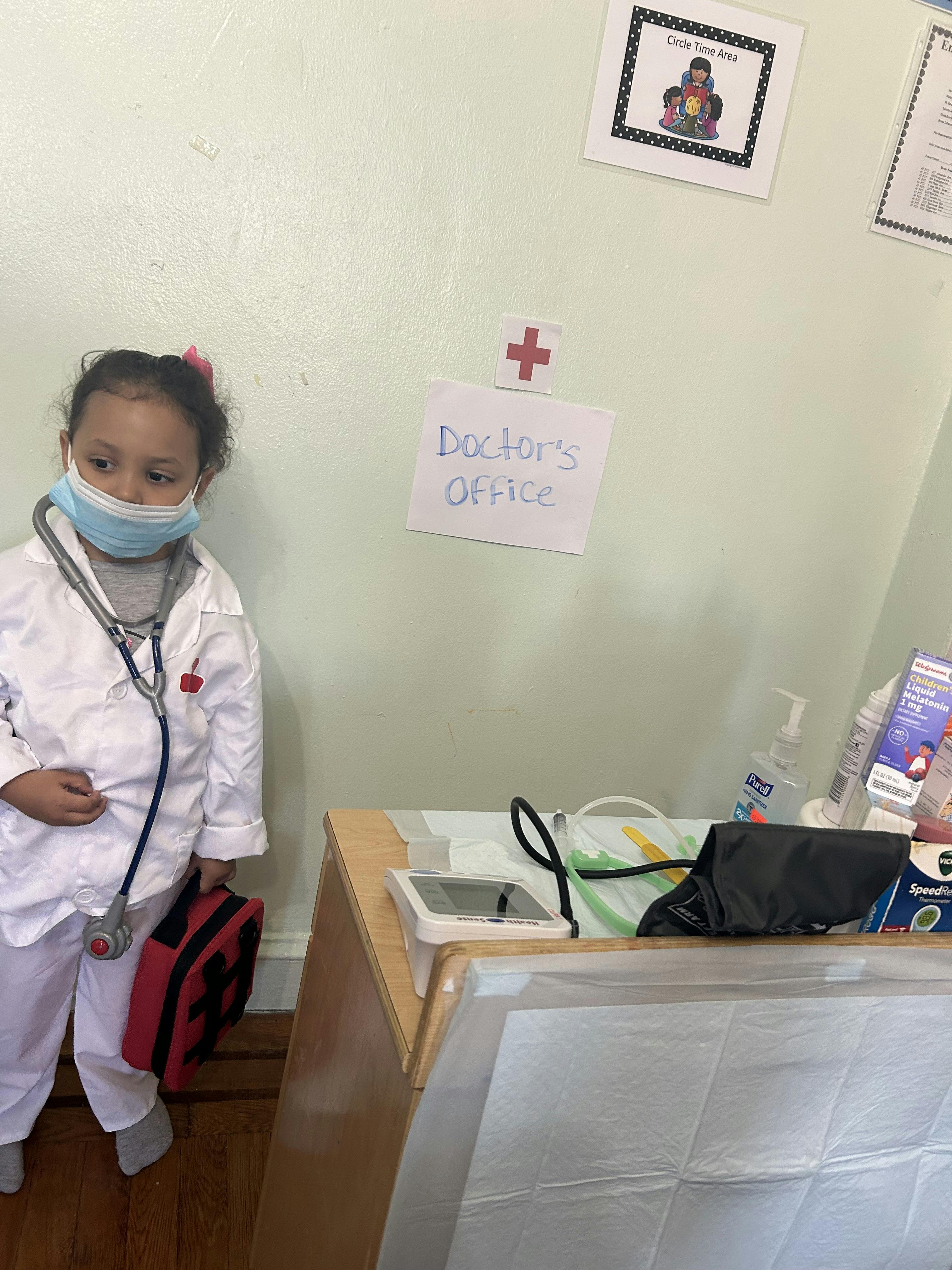 Child wearing a lab coat and face mask in a pretend doctor's office