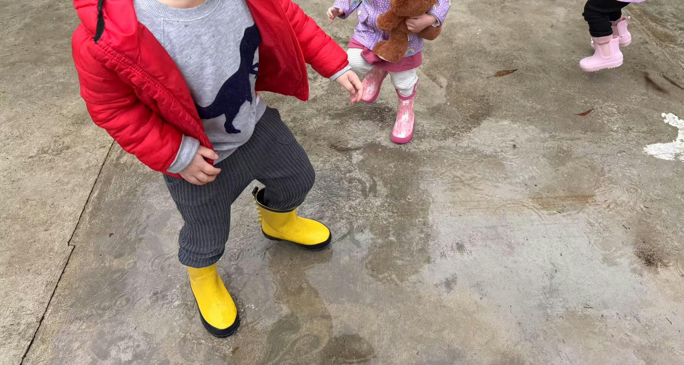 Child in red jacket and yellow boots standing on wet ground