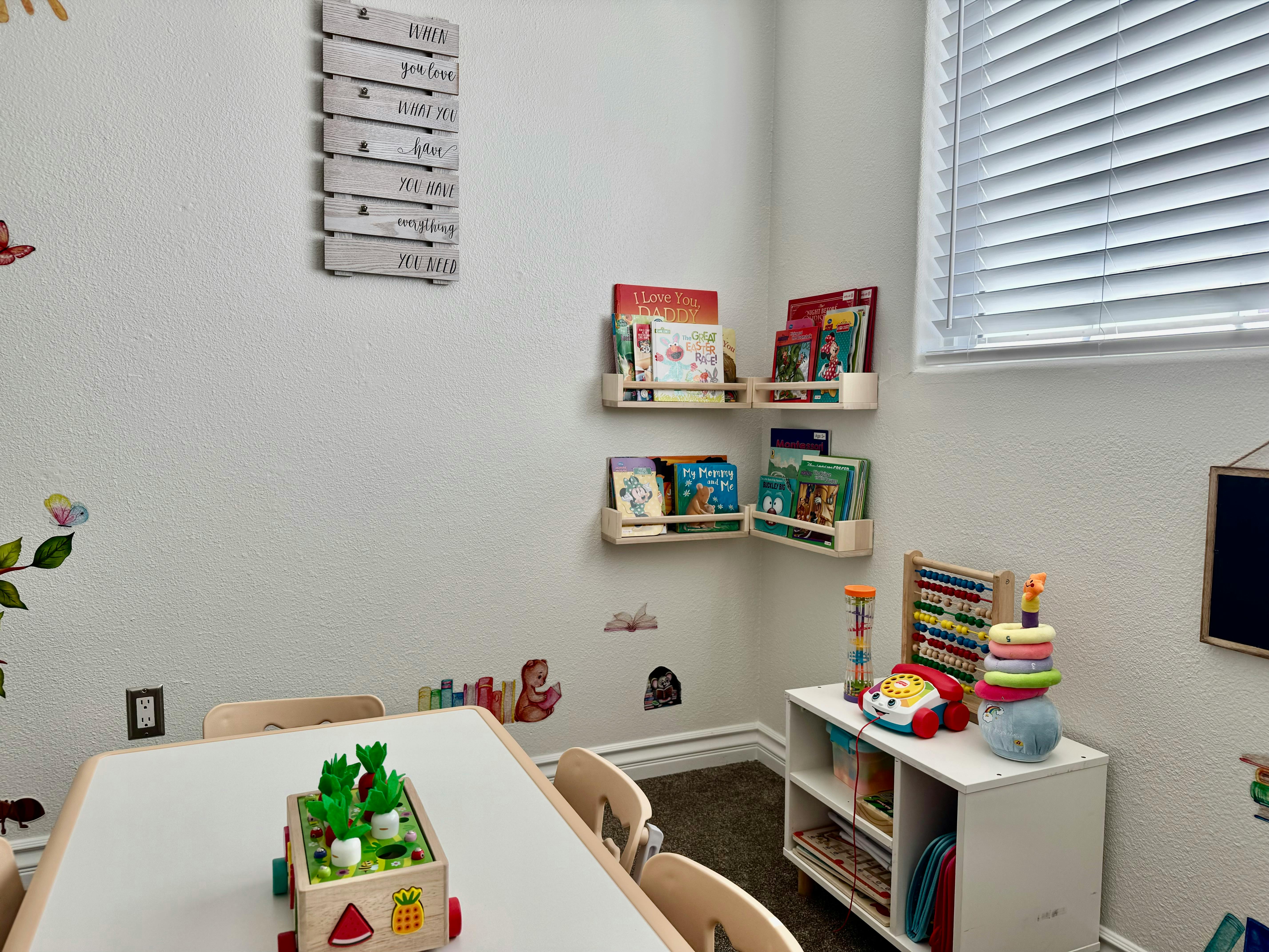 Children's room with small table, chairs, wall shelves with books, and toys