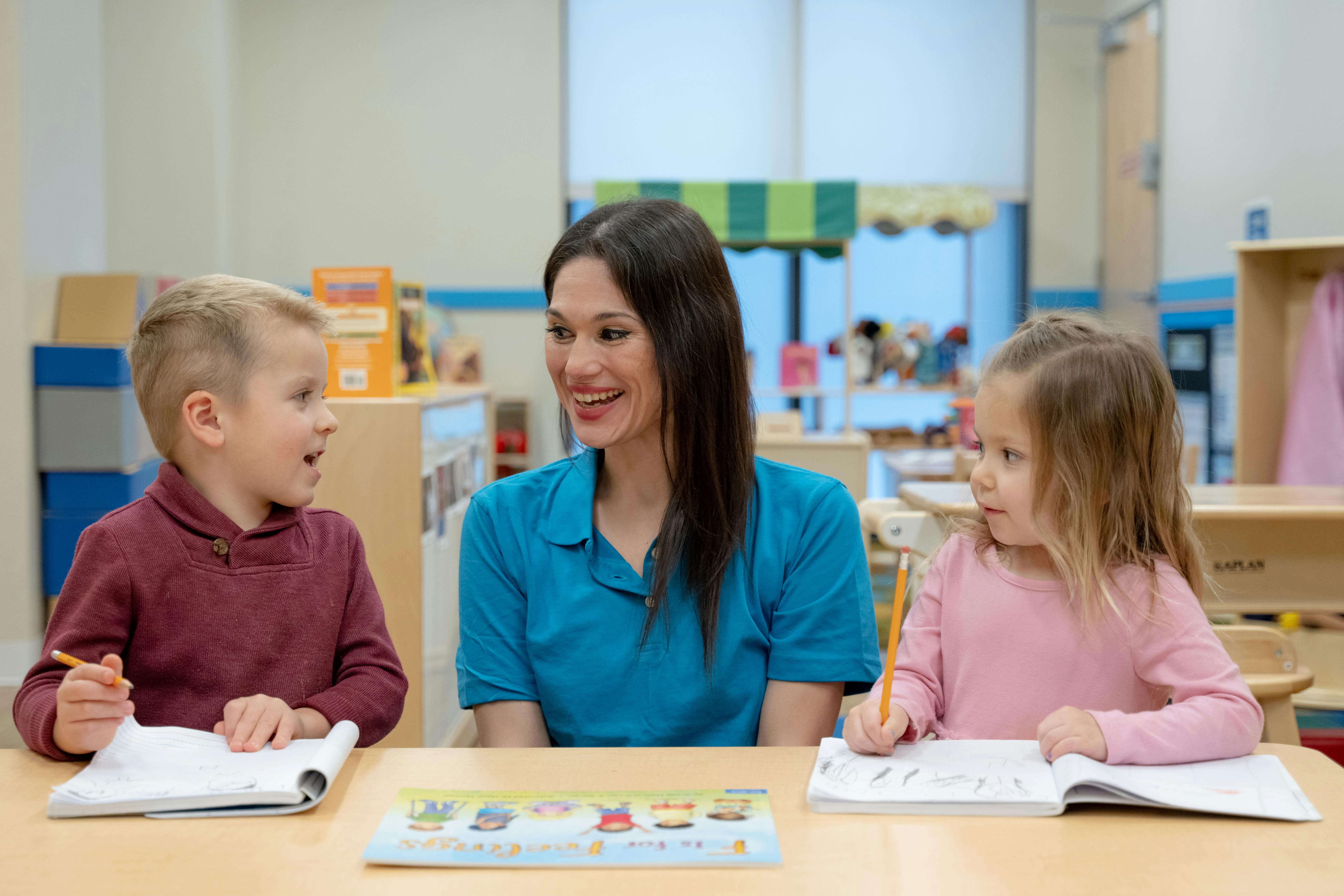 Adult and two children at a table with notebooks in a classroom