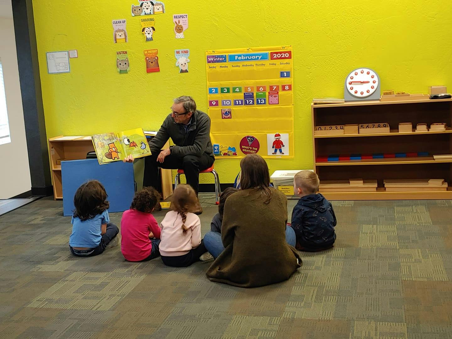 Person reading a book to children and an adult in a classroom