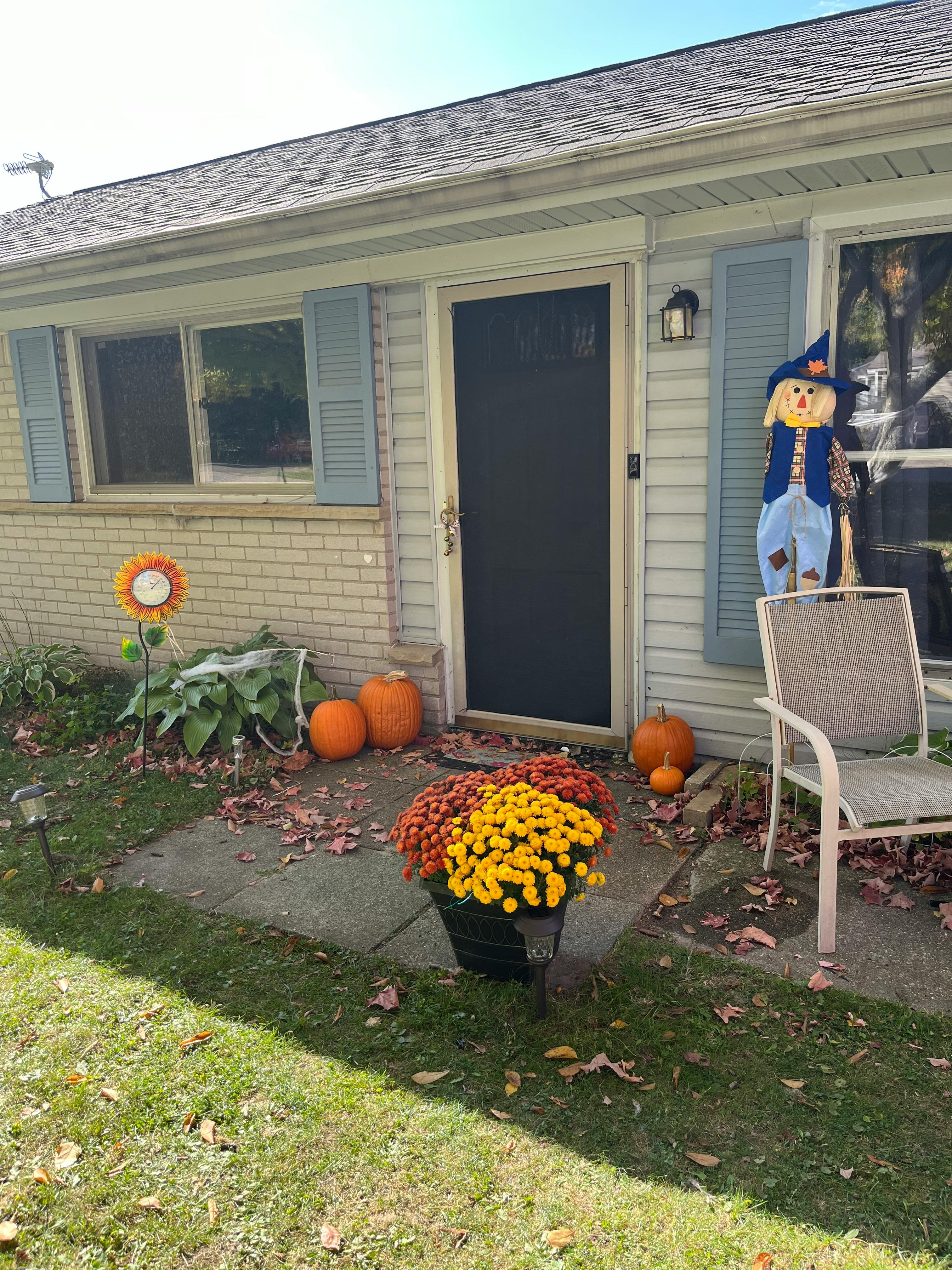 House entrance decorated with pumpkins, mums, and a scarecrow