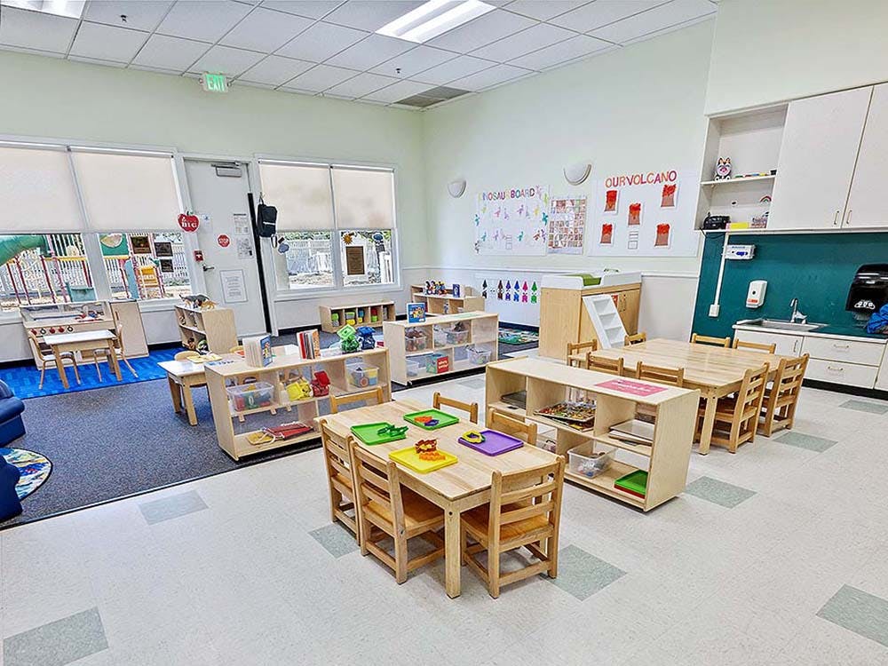 An empty early childhood classroom with multiple wooden tables and chairs