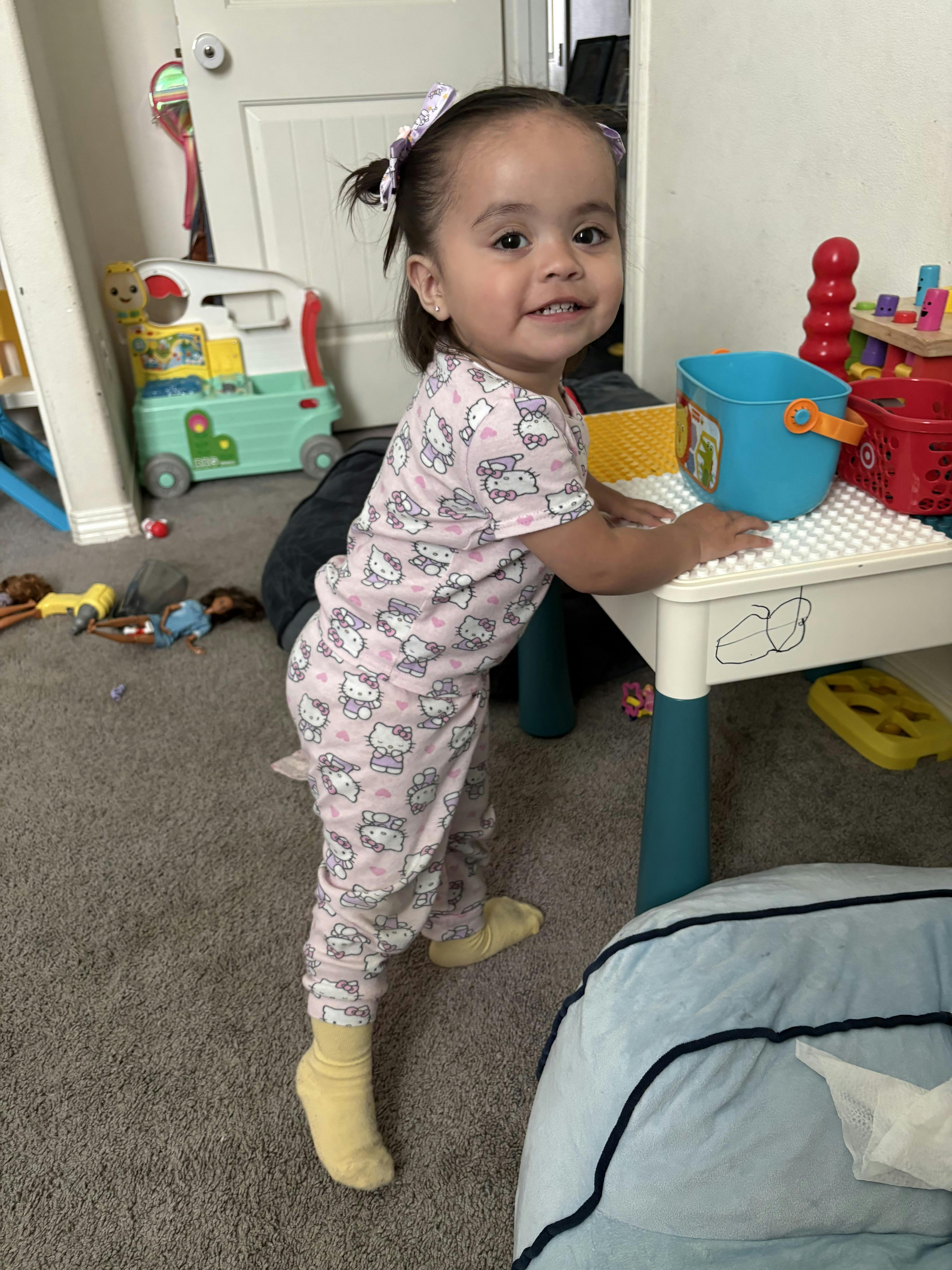 Child standing at a small play table in a room with toys
