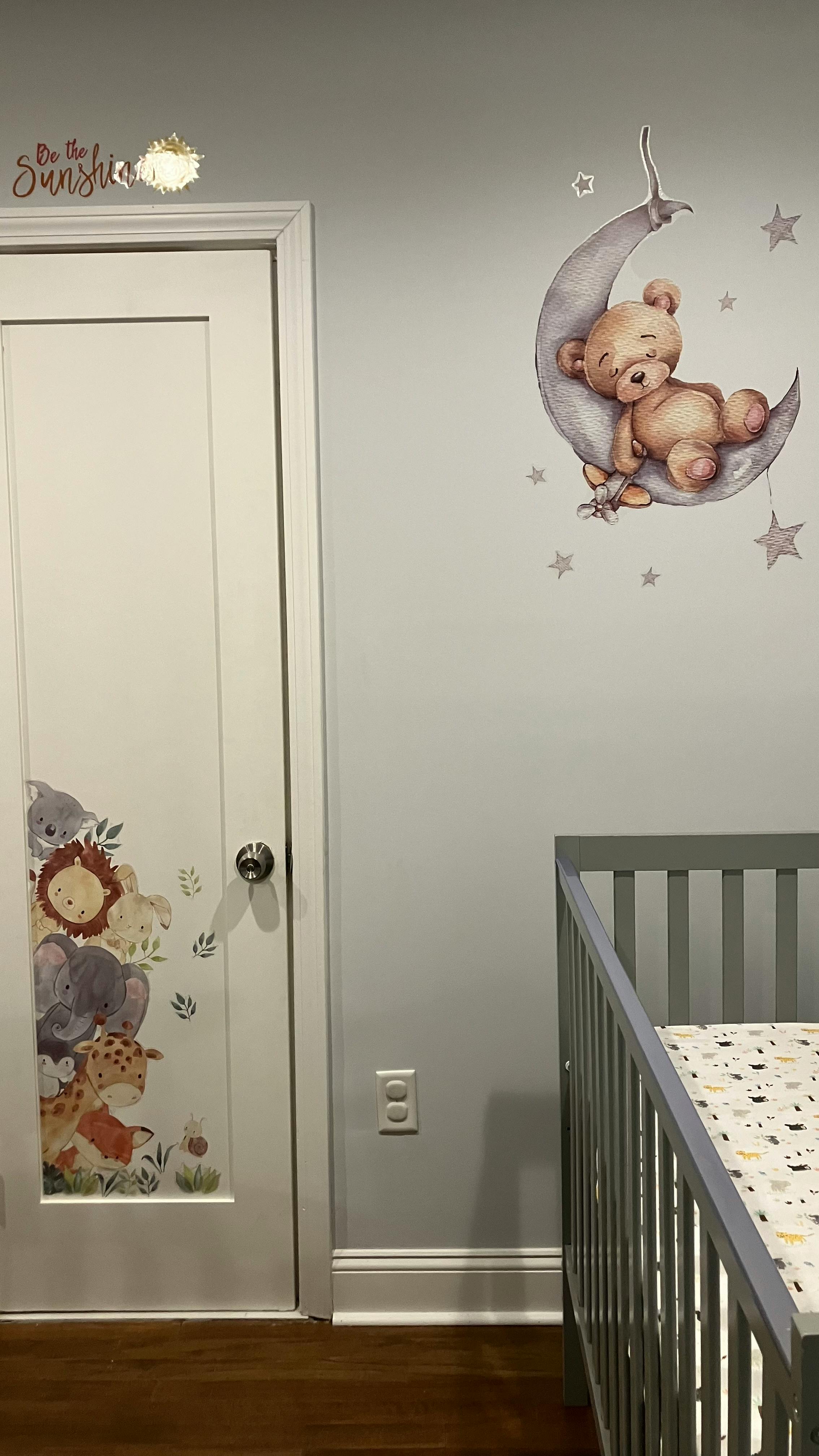 Nursery with a crib, door with animal decals, and a teddy bear on moon wall decal