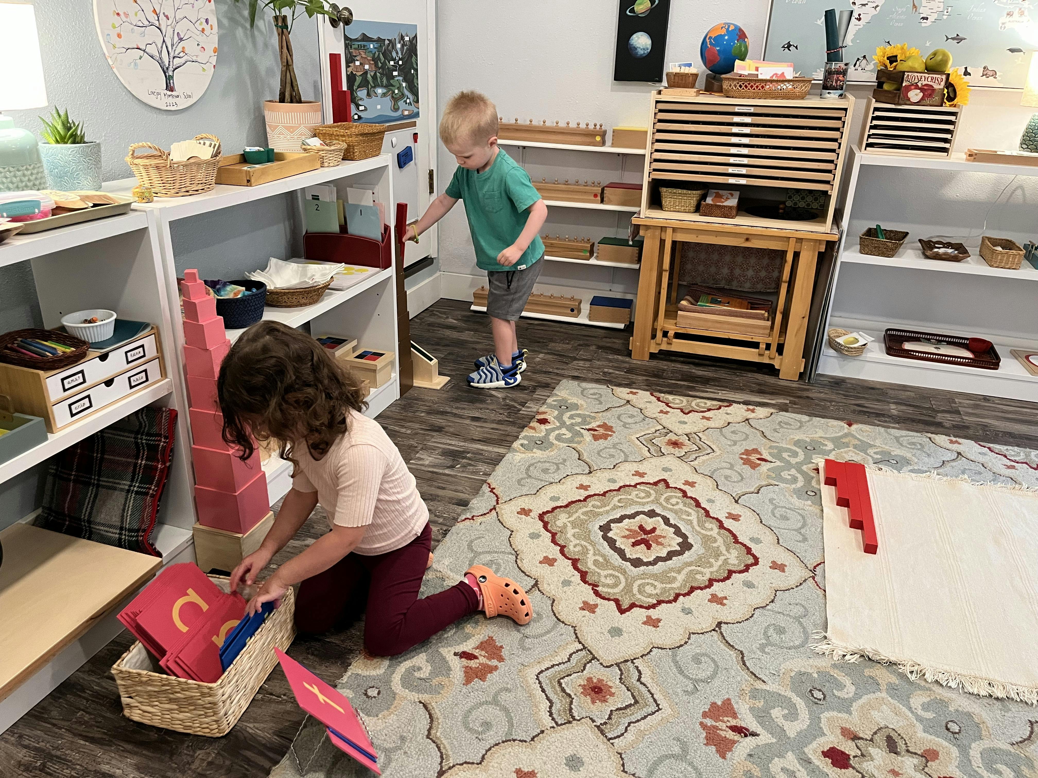 Child kneeling to sort red letter cards from a basket, another child standing near shelves