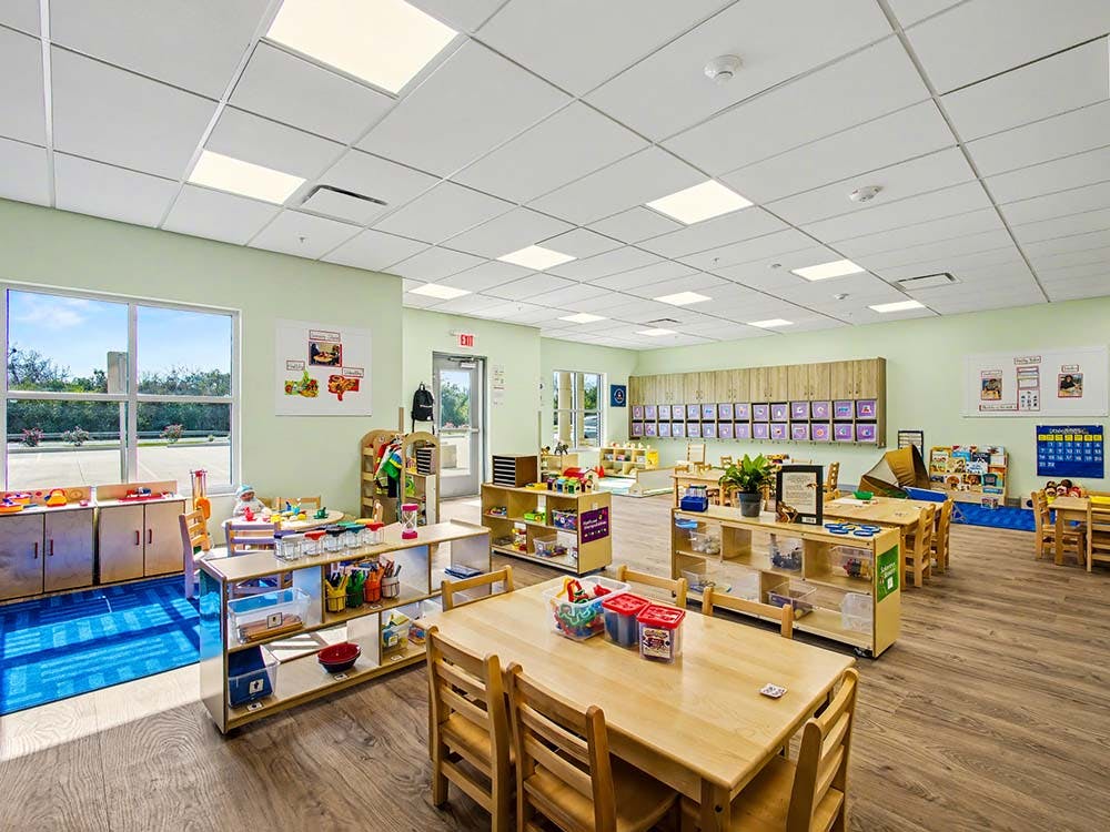 Spacious, brightly lit preschool classroom with light wood tables and chairs