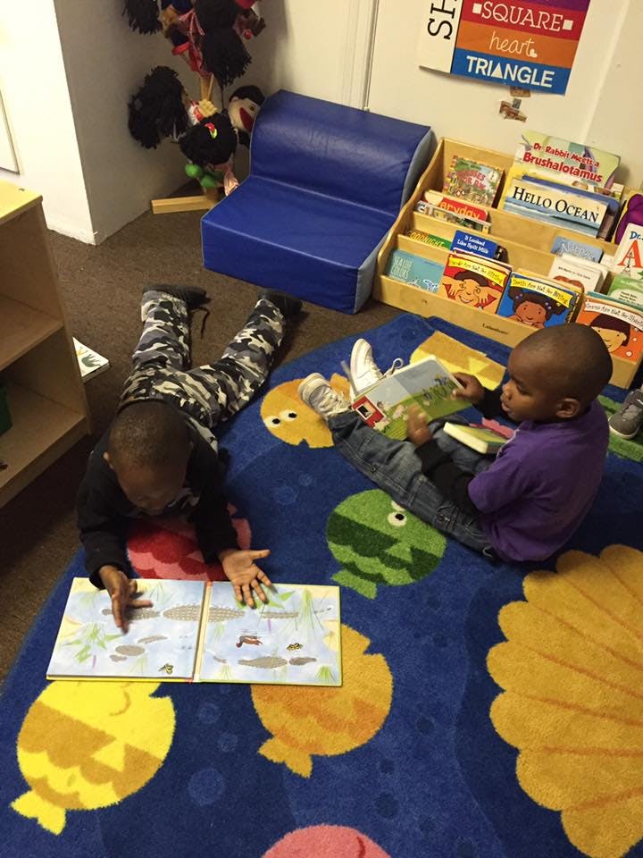 Two children reading books on a rug in a classroom