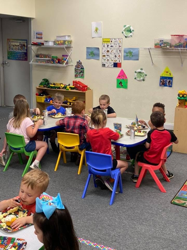 Children sitting at tables eating food in a classroom eating