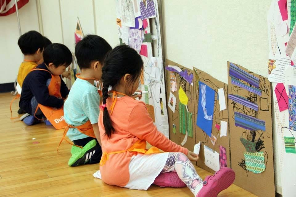 Children in aprons sitting on the floor creating art projects